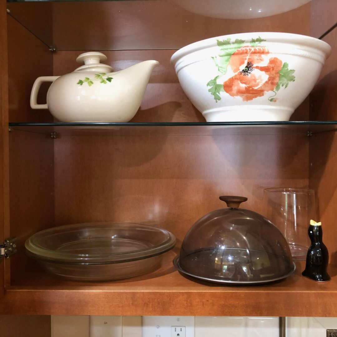 A glass shelf in a kitchen with several bowls and a teapot